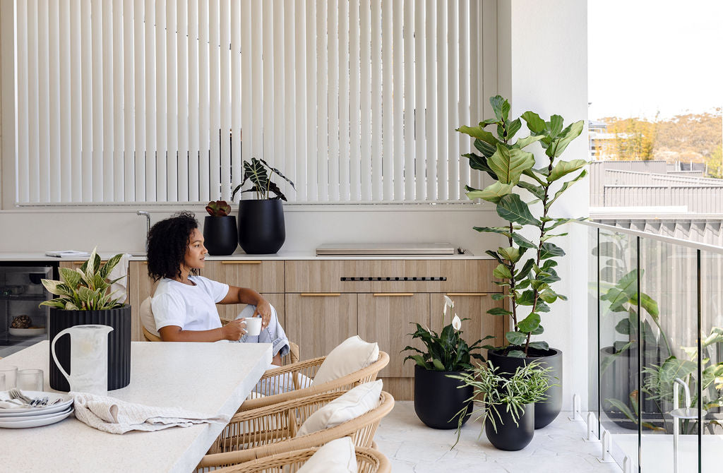 Woman enjoying her urban balcony retreat with modern black Slugg planters and lush green foliage